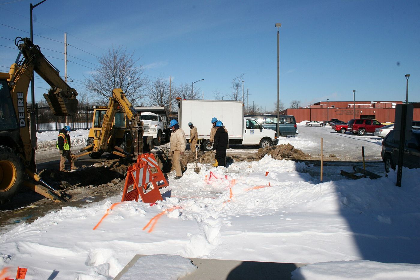 Utility workers repair large water pipes in a dug-up city street.