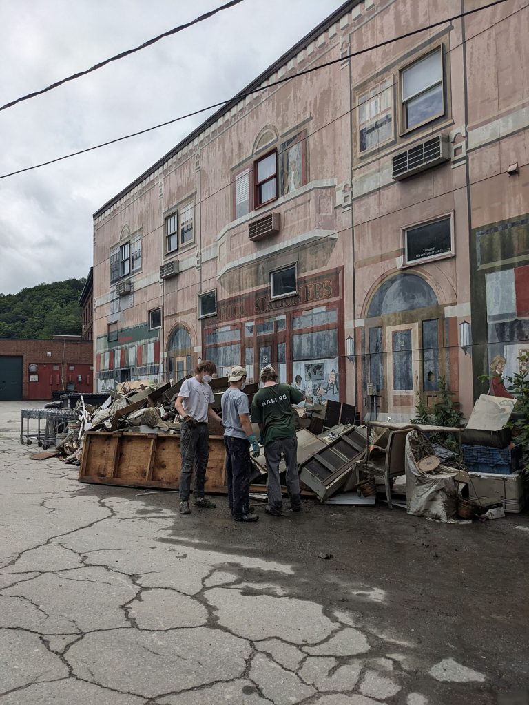 Cleanup workers clearing mud and debris from a flooded street after heavy rain in a neighbourhood.